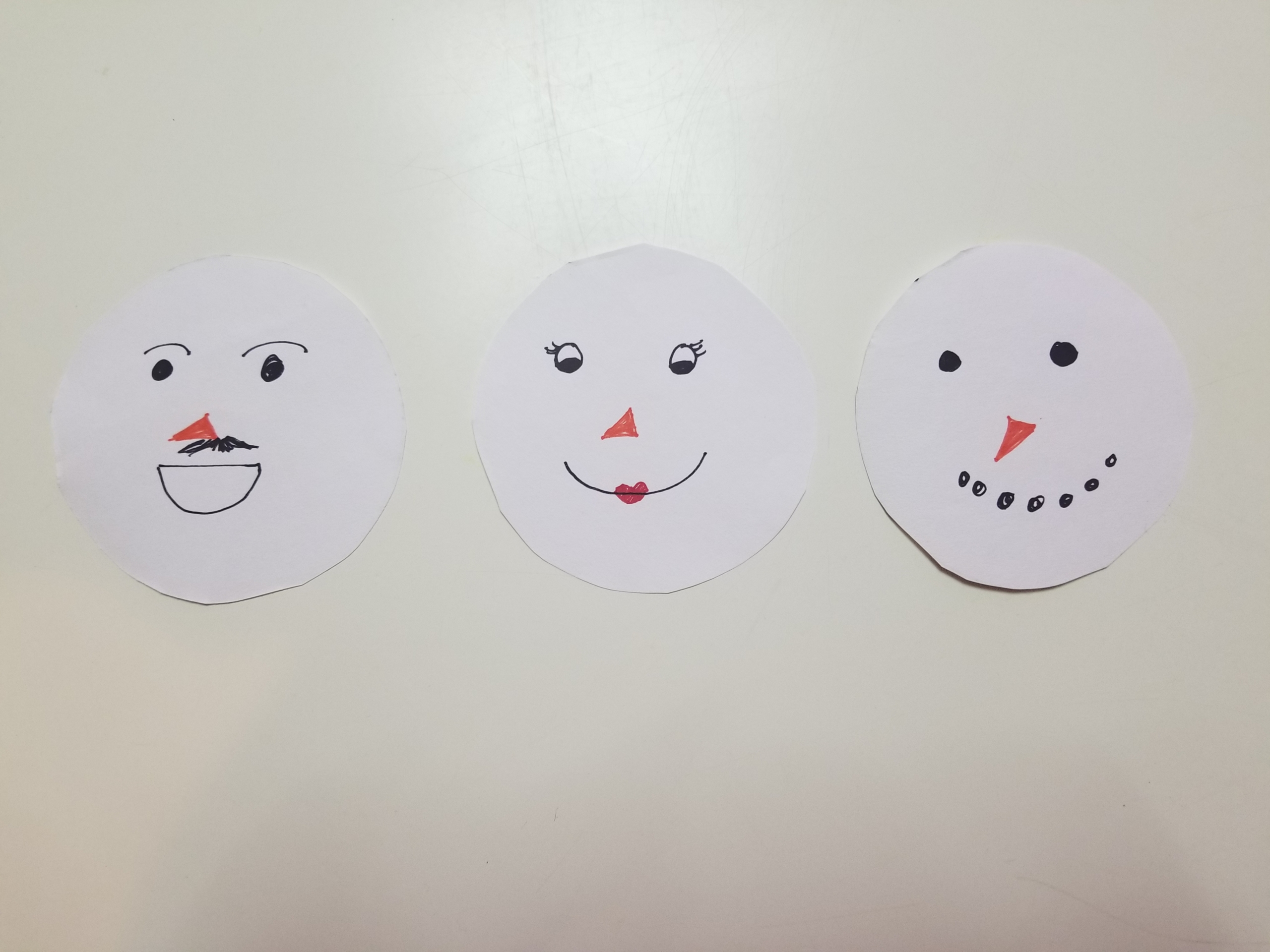 Three white paper circles with faces drawn on them