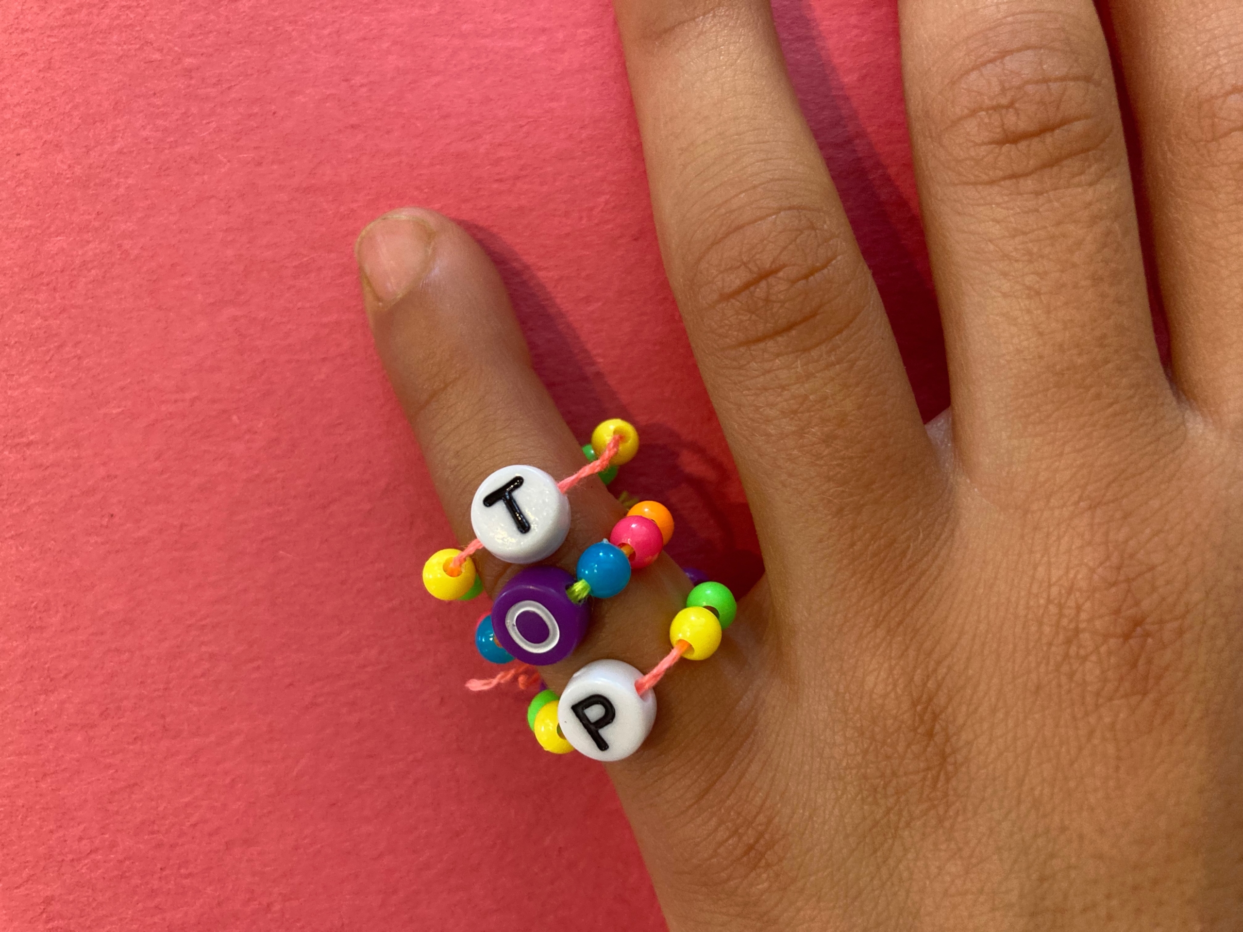 child wearing three bead rings that spells out 'Top'